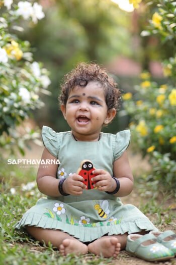 Baby girl wearing pastel green handpainted kids wear dress with floral and bee artwork